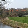 Das Kloster Marienwerder in Hannover von Ferne betrachtet mit einem Bachlauf im Vordergrund.