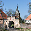 Ein Torbogen aus hellem Stein, der restauriert worden ist. Im Hintergrund ist ein Kirchturm zu sehen.