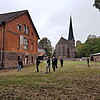 Eine Gruppe von sieben Personen läuft über das Stiftsgelände in Ilfeld, im Hintergrund ist eine Kirche zu sehen, vorne links ein mehrstöckiges Backsteingebäude.