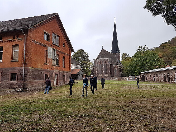 Eine Gruppe von sieben Personen läuft über das Stiftsgelände in Ilfeld, im Hintergrund ist eine Kirche zu sehen, vorne links ein mehrstöckiges Backsteingebäude.