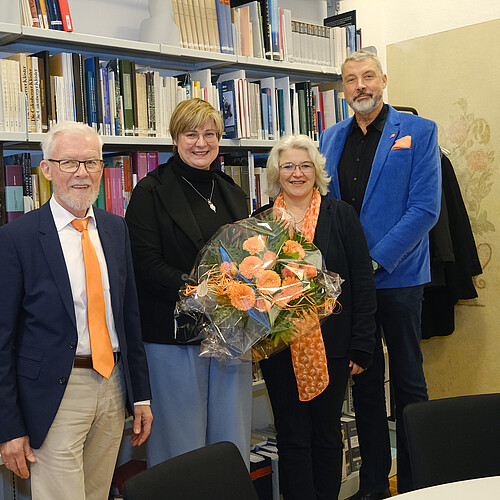 Vier Personen stehen in einer Bibliothek vor Bücherregalen.