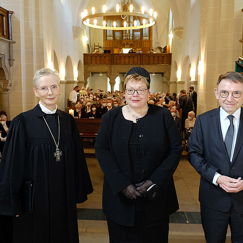Zwei Frauen und ein Mann stehen vor vollbesetzten Kirchenbänken in der Klosterkirche Marienwerder.