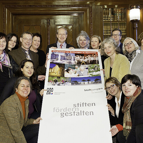 Eine Gruppe von Personen hält ein Werbebanner in den Händen mit der Überschrift: Wegweiser zu Stiftungen in Hannover.