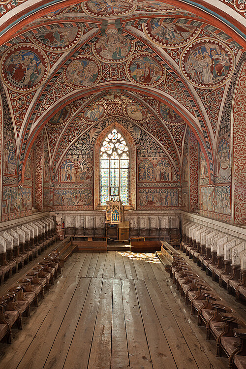 Man sieht einen Raum in einer alten Kirche, der komplett mit Holz ausgestaltet ist. Die Decke ist kunstvoll bemahlt.