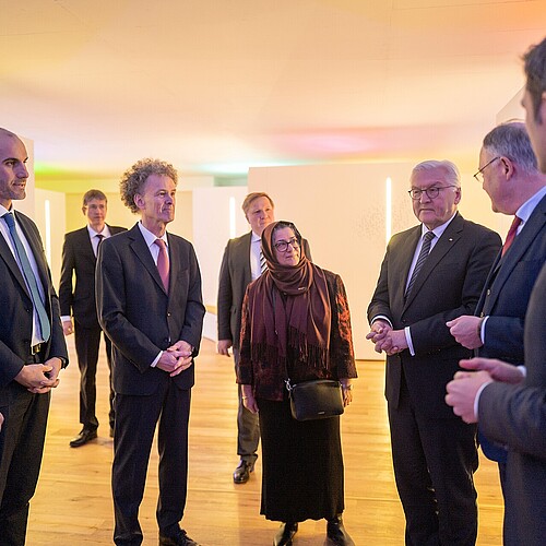 Neun Personen stehen in einem Halbkreis in einem Ausstellungsraum, der in hellen Farben gestaltet ist.