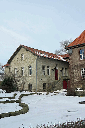 der Blick auf den Eingangsbereich aus etwas Entfernung, im Vordergrund ist ein schneebedeckter Weg zu sehen.