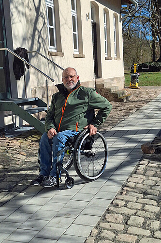 Ein Mann im Rollstuhl steht auf einem Weg neben einem Gebäude.