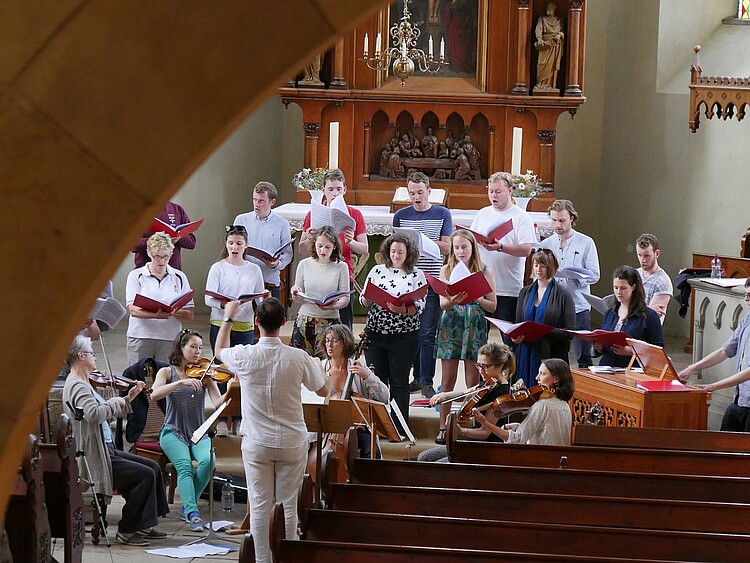 Eine Gruppe von jungen Frauen und Männern hat sich vor einem Altar versammelt, sie singen und spielen auf Instrumenten.