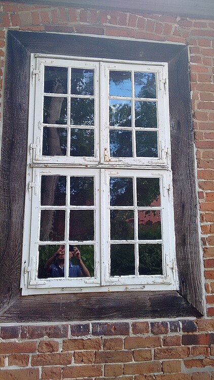 Blick auf ein historisches Sprossenfenster mit hölzerner Umrahmung in einer Bachsteinwand.