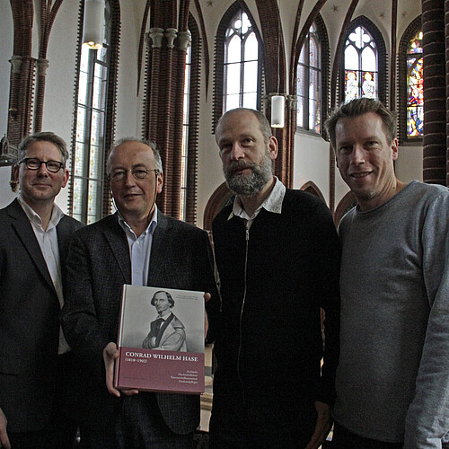 Vier Männer stehen nebeneinander in der Christuskirche in Hannover, einer von ihnen hält ein Buch in den Händen.