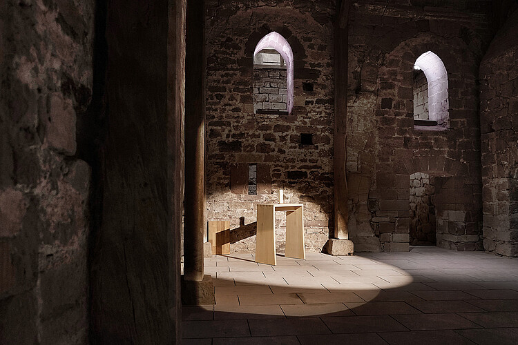 Blick in den Hauptraum des Westbaus der Stiftskirche Fredelsloh: Auf dem Steinfußboden stehen wenige Holzmöbel. Die Wände sind unverputzt, die Spitzbogenfenster unverglast.