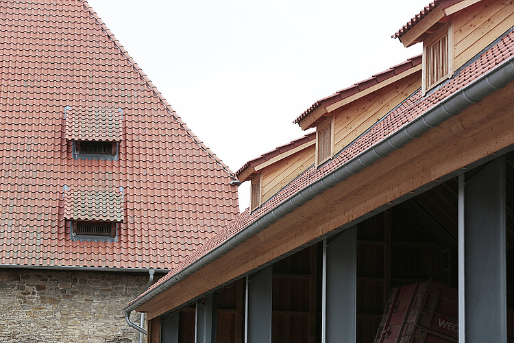 Blick auf das neue Ziegeldach der Halle neben dem alten Dach des angrenzenden Gebäudes.