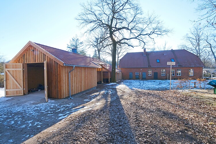 Nebengebäude aus Holz im Vordergrund; quer dazu ein Steingebäude