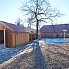 Nebengebäude aus Holz im Vordergrund; quer dazu ein Steingebäude