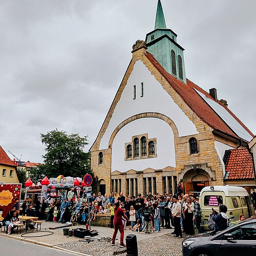 Eine Moderne Kirche mit Turm, davor sind viele Menschen versammelt.