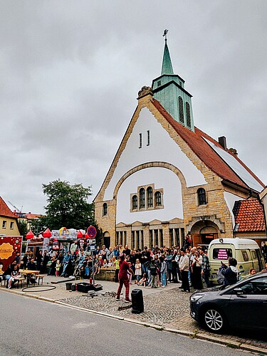 Eine Moderne Kirche mit Turm, davor sind viele Menschen versammelt.