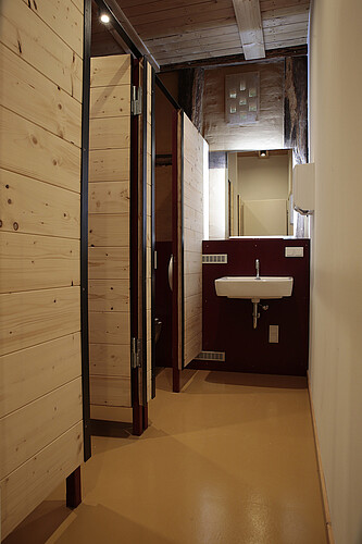 Blick in die neu eingebaute Toilettenanlage mit Waschbecken und Spiegel sowie zwei WC-Kabinen.