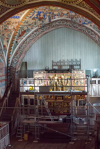 Unterhalb einer aufwändig verzierten Gewölbedecke steht ein filigraner Altaraufsatz, vor dem ein Gerüst zum Restaurieren aufgebaut ist.