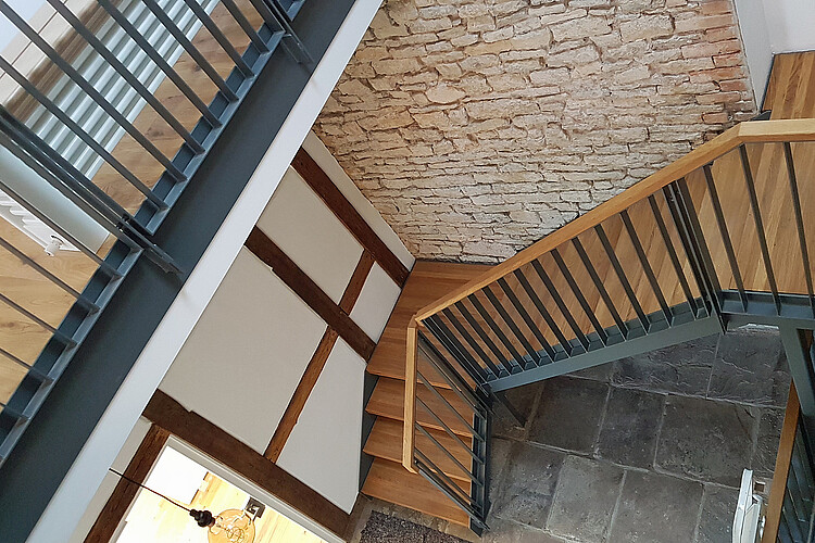 Blick von oben auf eine moderne Stahltreppe mit Eichenholzstufen, die innen zwei Etagen in dem Molkehaus verbindet.