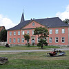 Leicht schräge Gebäudeansicht mit angeschnittener Mauer rechts und ein Stück des Kirchturms im Hintergrund links.