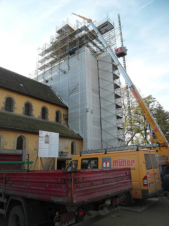 Vor einem eingerüsteten Kirchturm steht ein hoher Baukran.