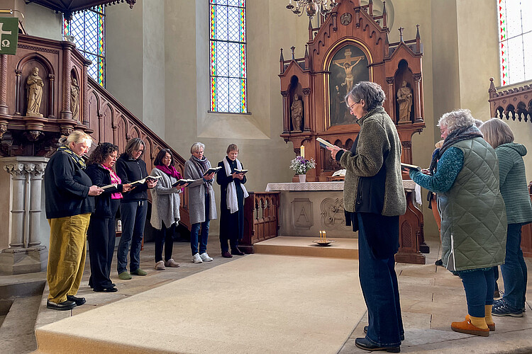 Eine Runde von Frauen mit Gesangsbüchern steht vor einem Altar.