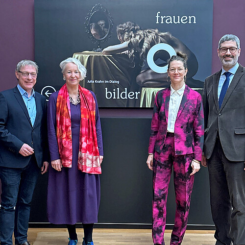 Vier Personen vor einen Ausstellungsplakat