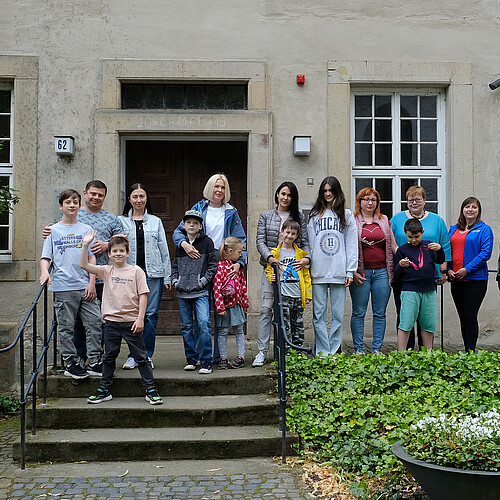 Eine Gruppe geflüchteter Menschen aus der Ukraine steht zusammen mit Äbtissin Ulrike Kempe vor dem Haupteingang zum Kloster Marienwerder.
