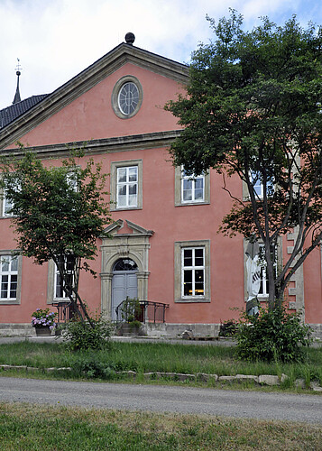 Eingangsbereich von außen betrachtet, mit Bäumen im Vordergrund.