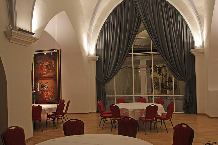 Runde große Tische mit roten Stühlen stehen in einem Raum mit einer weißen Gewölbedecke.