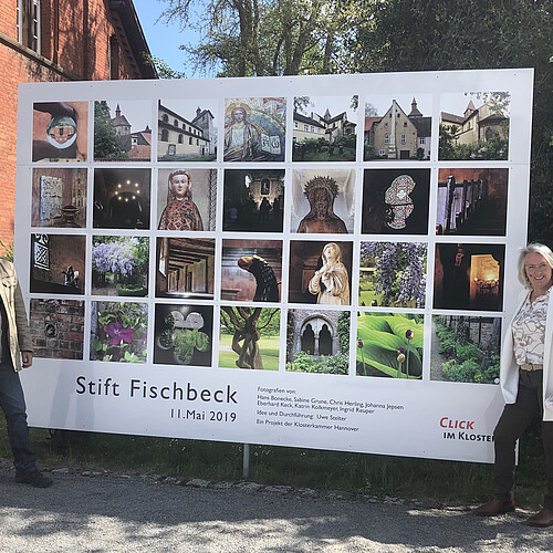 Ein Mann und eine Frau stehen an zwei Seiten einer großformatigen Fotoinstallation mit Bildern aus dem Stift Fischbeck.