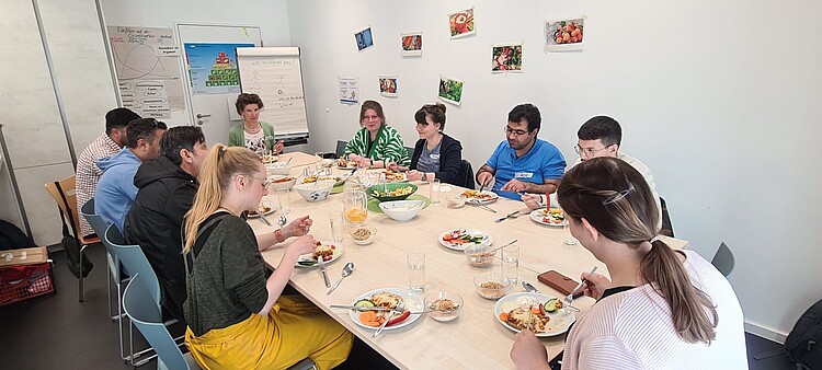 Gruppe überwiegend jüngerer Menschen beim Essen in einem Seminarraum