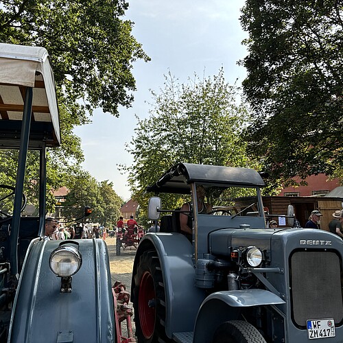 Zwei historische blaugraue Traktoren stehen auf einem großen Hofgelände.