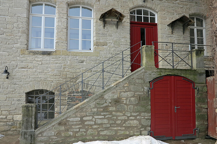 Detailansicht der sanierten Natursteintreppe, die zur dunkelroten Eingangstür hinauf führt.