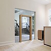Ein heller Raum mit verglaster Tür der in einen Eingangsbereich übergeht.
