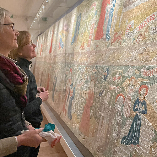 Zwei Frauen stehen vor einer Vitrine mit kostbaren, jahrhundertealten Teppichen im Museum des Klosters Wienhausen.