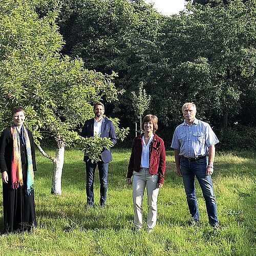 Vier Personen stehen auf einer Wiese zwischen Bäumen.