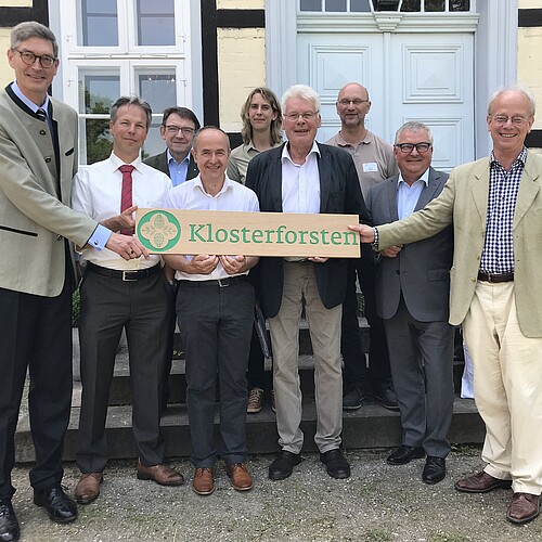 Neun Personen stehen als Gruppe vor einem Fachwerk-Gebäude.