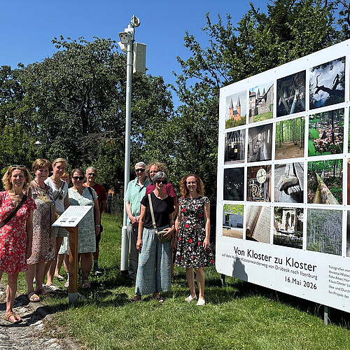 Eine Gruppe von zehn Personen steht neben einer großformatigen Installation mit Fotos.