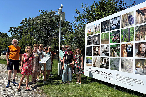 Eine Gruppe von zehn Personen steht neben einer großformatigen Installation mit Fotos.
