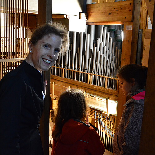 Eine Frau und zwei Kinder im Inneren einer Orgel. Blick auf Orgelpfeifen.