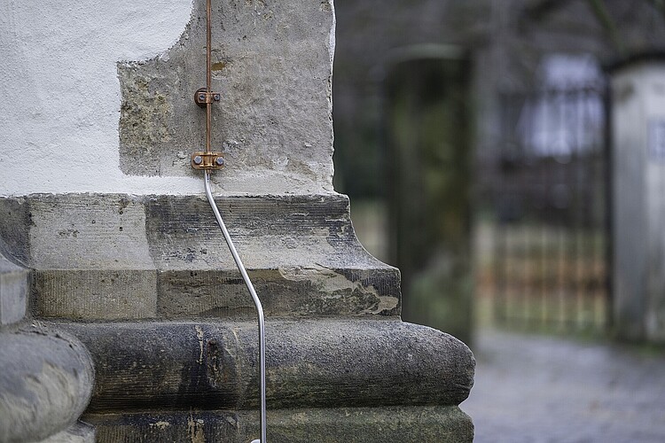 Detailansicht die zeigt, wie ein Metallelement als Blitzschutz an der Außenfassade der Kirche befestigt ist.