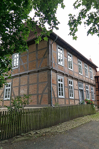 Blick von der Seite auf ein restauriertes Fachwerk-Gebäude mit einem hölzernen Zaun davor.