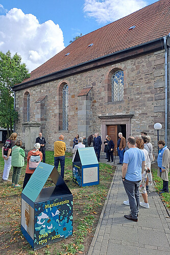 Eine Gruppe Menschen nimmt an einer Kirchenführung teil und steht vor dem Bauwerk.