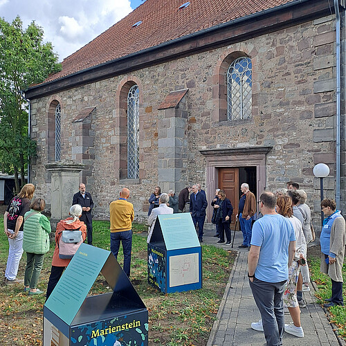Eine Gruppe Menschen nimmt an einer Kirchenführung teil und steht vor dem Bauwerk.