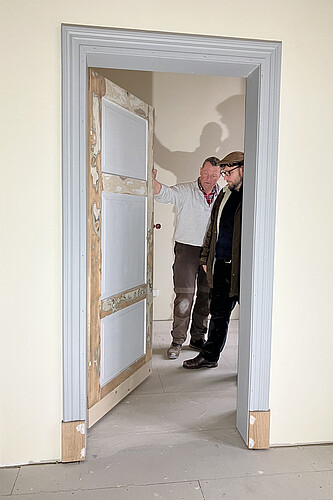 Zwei Männer stehen in einer halb geöffneten Tür und schauen sich an, wie diese aufgearbeitet worden ist.