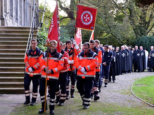 Eine Gruppe Personen geht in Dreierreihen einen Weg entlang.