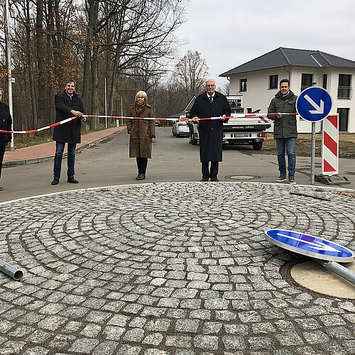 Vier Männer und eine Frau stehen auf einer neu angelegten Straße und halten ein rot-weißes Band in den Händen.