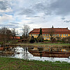 Auf einer Wiesenfläche hat sich Wasser aufgestaut, dahinter ist ein Gebäude des Klosters Mariensee mit gelber Fassade und rot gedecktem Dach zu sehen.