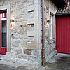 Eine Außenwand aus hellem Stein mit einer roten Eingangstür aus Holz.